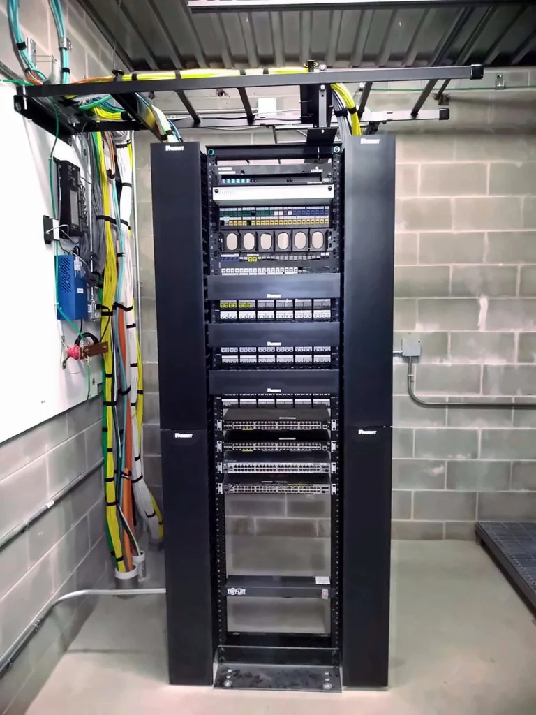 Network rack with patch panels, switches, and vertical cable managers in a telecom room