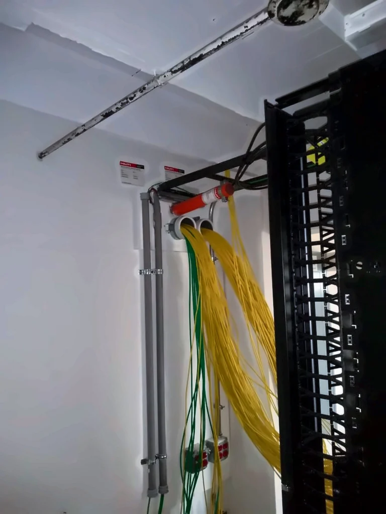 Cable bundles entering a room through wall sleeves beside a rack